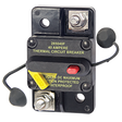A black surface mount thermal circuit breaker with a red switch lever and a yellow wire terminal. It has text indicating the model number, amperage rating, and a warning that it is ignition protected and water resistant.